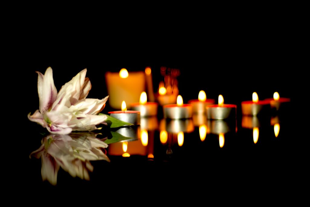 White lily, candles of a funeral on a plaque with the reflection of lights. Mourning background